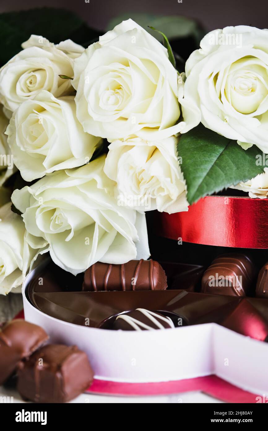 Roses blanches avec bonbons au chocolat mélangés pour la Saint-Valentin.Mise au point sélective avec un premier plan et un arrière-plan flous. Banque D'Images