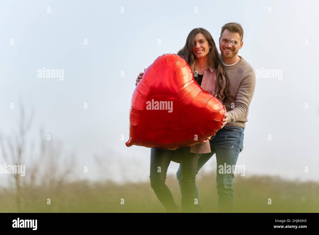 Jeune couple célébrant la Saint-Valentin en tenant une montgolfière rouge en forme de cœur Banque D'Images