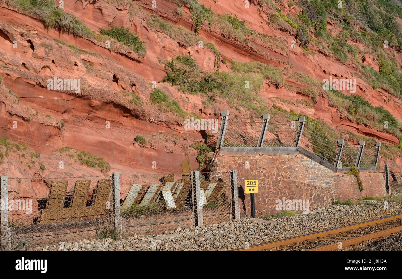 Falaises de grès rouge et filets de chute de roche le long de la ligne de chemin de fer côtière à Dawlish, dans le sud du Devon. Banque D'Images