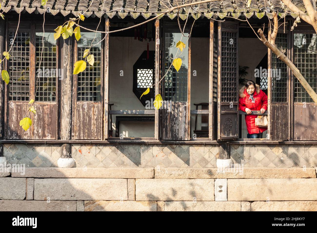Dame dans un manteau rouge penchée hors de la fenêtre d'une ancienne demeure dans la ville aquatique de Zhouzhuang, Chine Banque D'Images