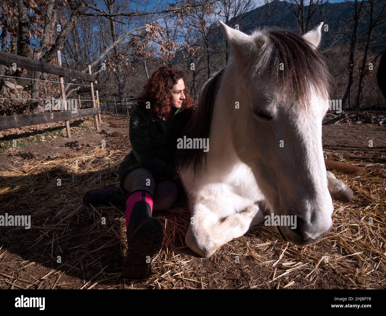 Vue latérale de la femme en veste polaire verte, assise sur le côté d'un poney blanc. Banque D'Images