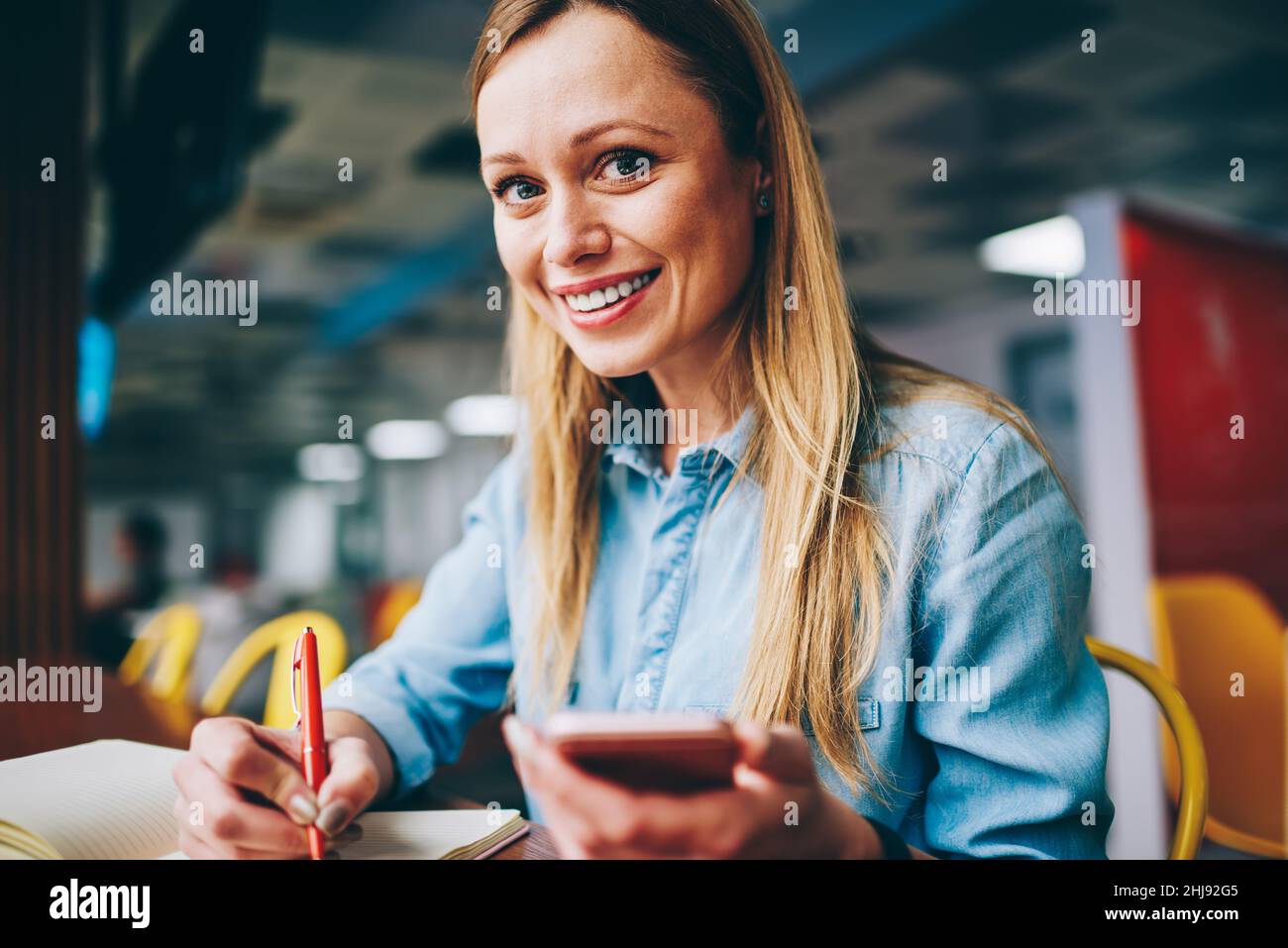 Une femme heureuse avec un smartphone qui prend des notes Banque D'Images