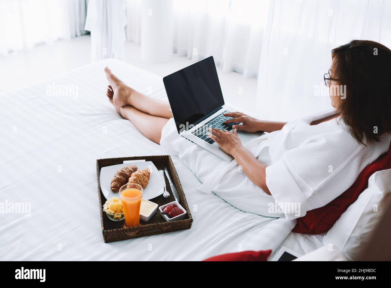 Young woman sitting on bed with laptop Banque D'Images