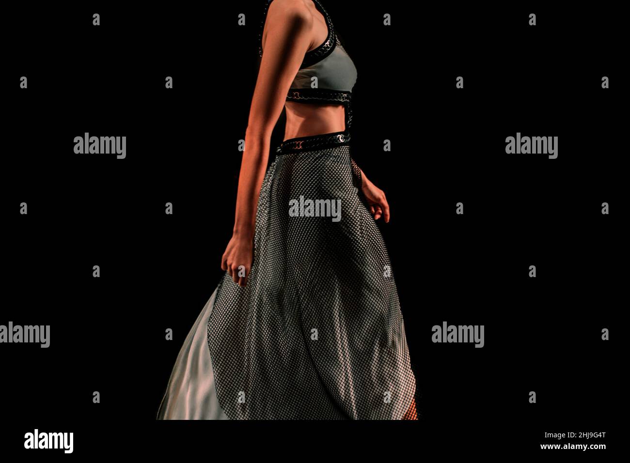 Femme habillée dans un ensemble gris boho jupe longue et brassière marche sur un fond noir.Détails de la mode Banque D'Images