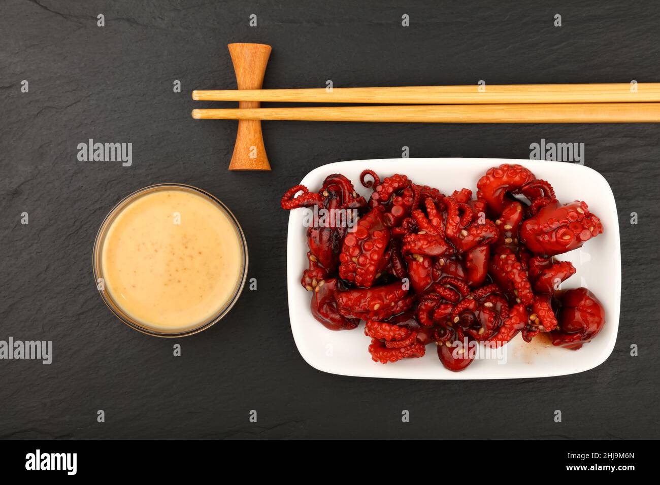 Gros plan de la petite salade de poulpes rouges entières de fruits de mer avec sauce satay et baguettes sur fond de tableau d'ardoise noire, vue du dessus en hauteur, dir Banque D'Images