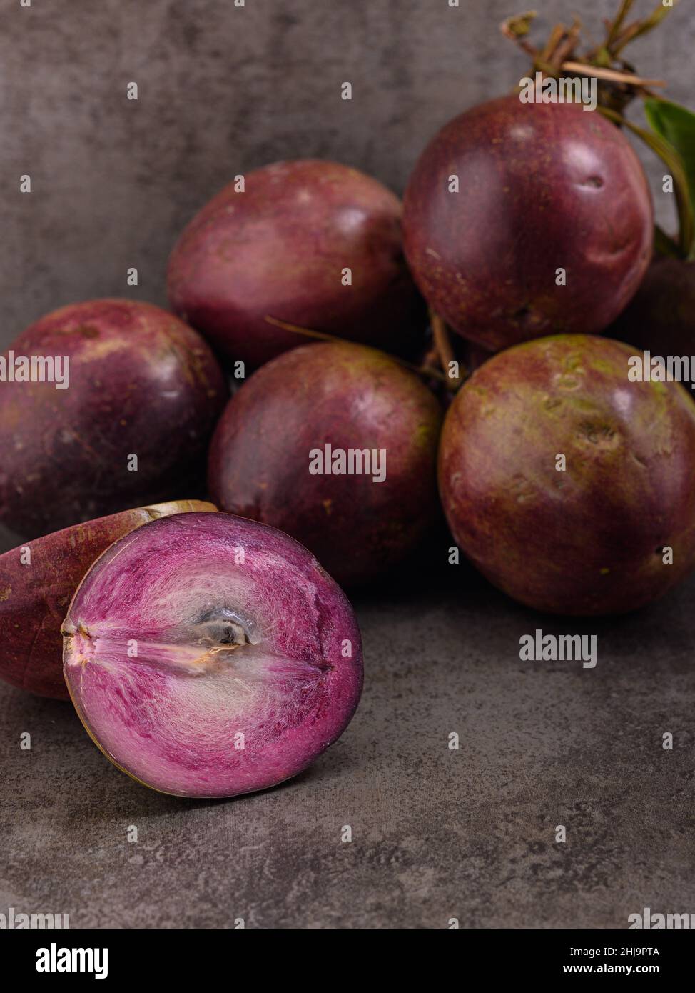 La photo montre plusieurs fruits tropicaux violets.Un fruit est coupé ouvert et l'intérieur est visible.Le fruit Caimito est originaire de la jungle du Repu dominicain Banque D'Images