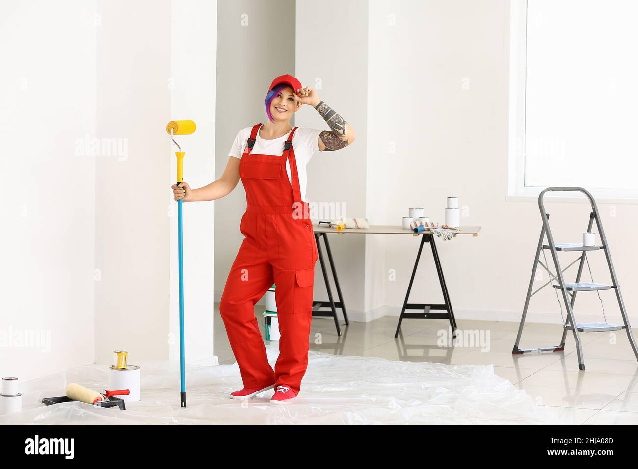 Femme peintre avec uniforme rouge et rouleau à peinture dans la chambre Banque D'Images