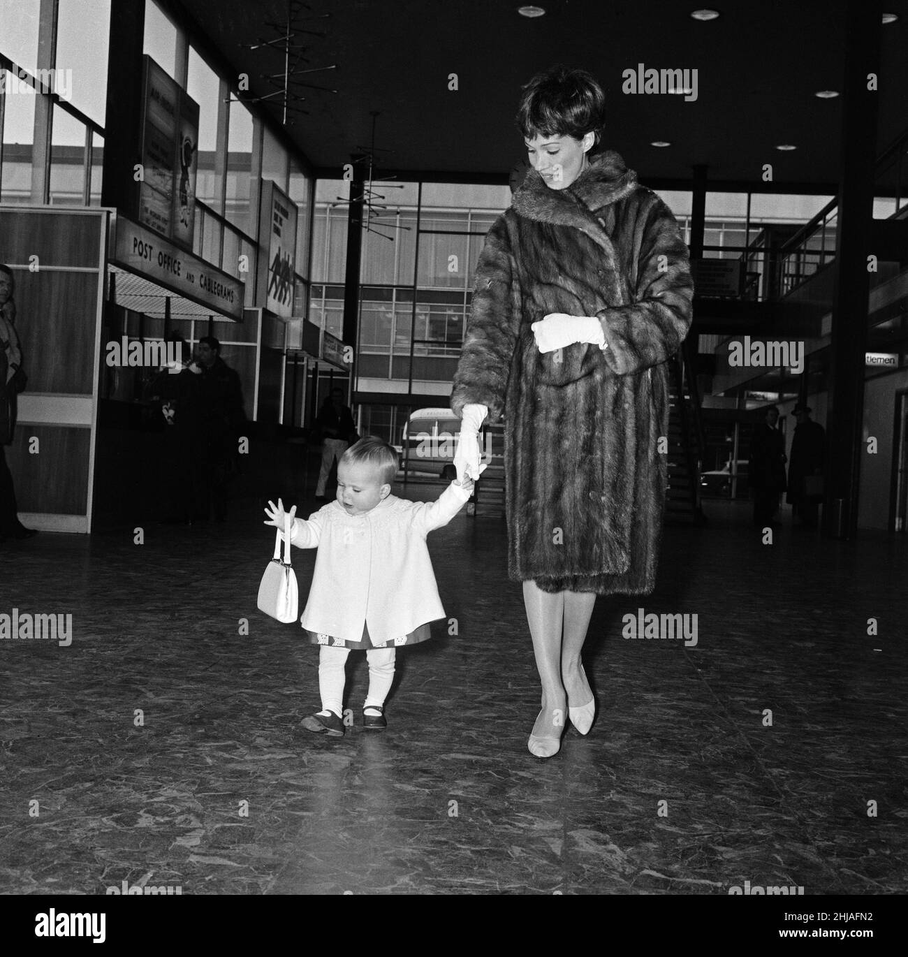 Julie Andrews et sa fille Emma quittent l'aéroport de Londres pour New York.La petite Emma avait la course de l'aéroport, et est allée à pied avec 'Cindy' un coolé.Elle a rencontré un petit garçon appelé Robin Coulson, âgé de 2 ans, et a dû l'embrasser Au revoir avant d'être finalement rouée dans un chariot à bagages.18th février 1964. Banque D'Images