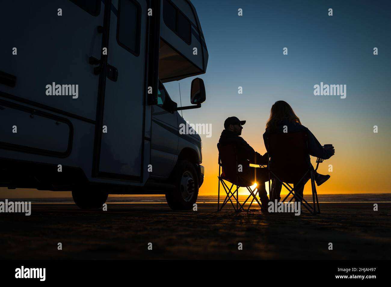 Couple caucasien se relaxant à côté de leur camping-car sur la plage de Pismo pendant le coucher de soleil panoramique.Thème de voyage en voiture de loisir. Banque D'Images