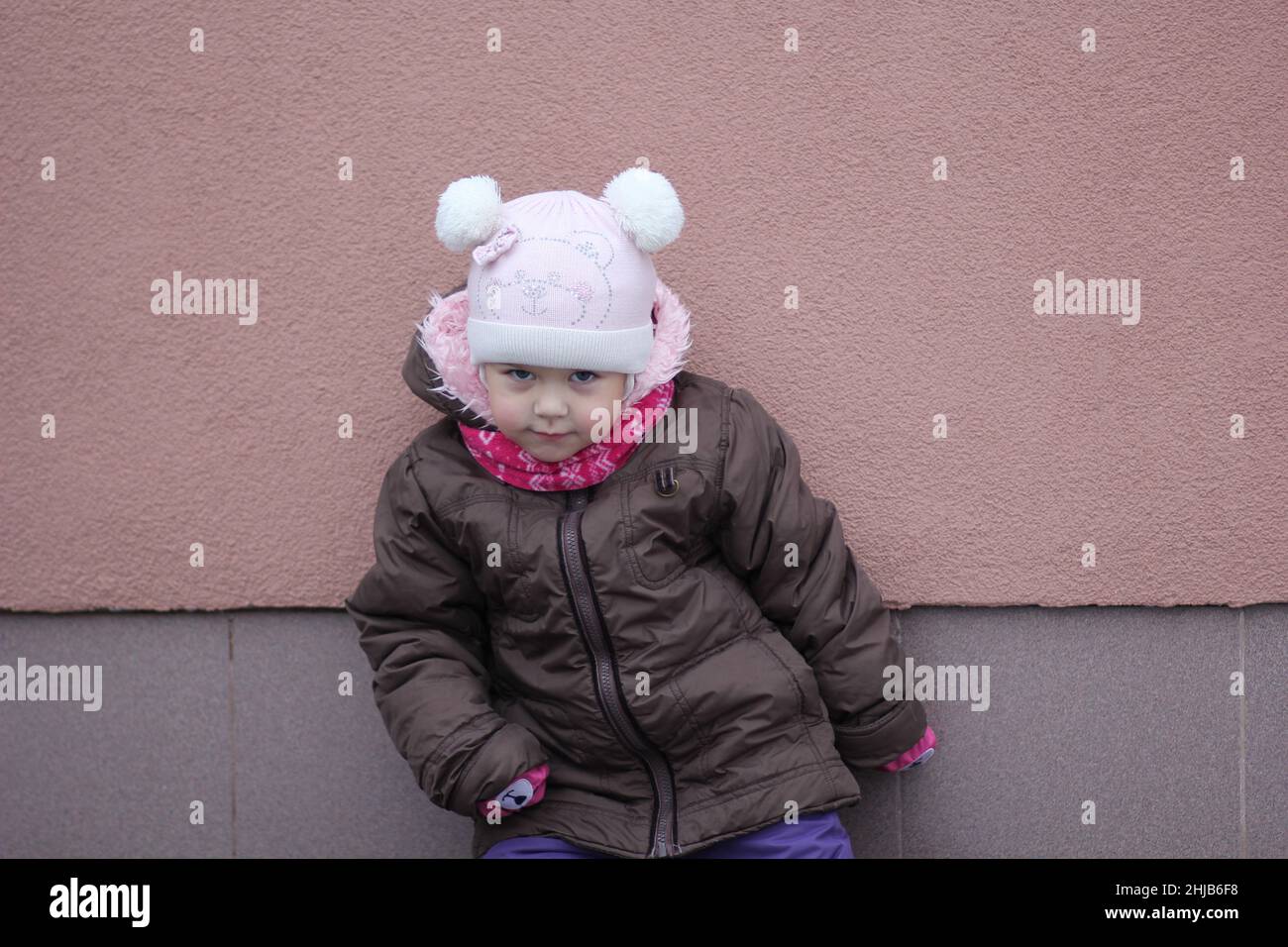 Enfant dans un tissu chaud en hiver regardant l'appareil photo debout dans la pose sur fond violet Banque D'Images