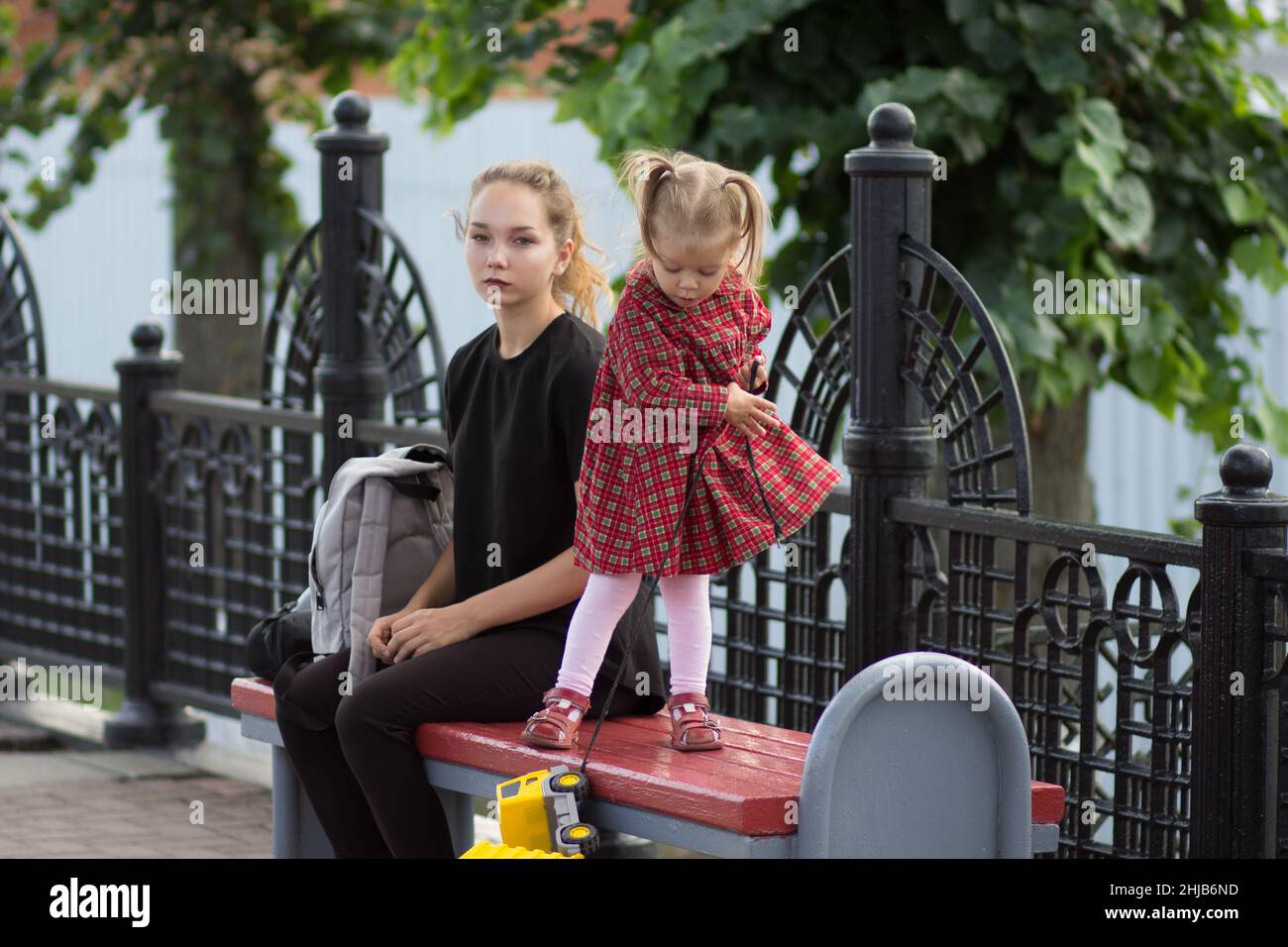 Jeune femme avec la pensée regarder assis sur le banc avec sac avec enfant de deux ans Banque D'Images