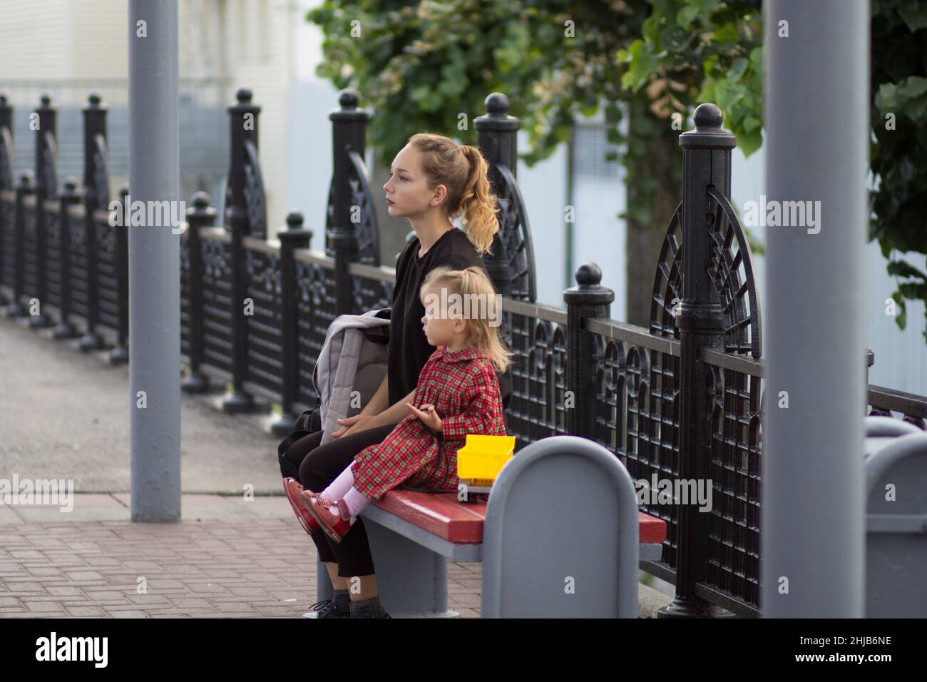 Jeune femme avec la pensée regarder assis sur le banc avec sac avec enfant de deux ans Banque D'Images