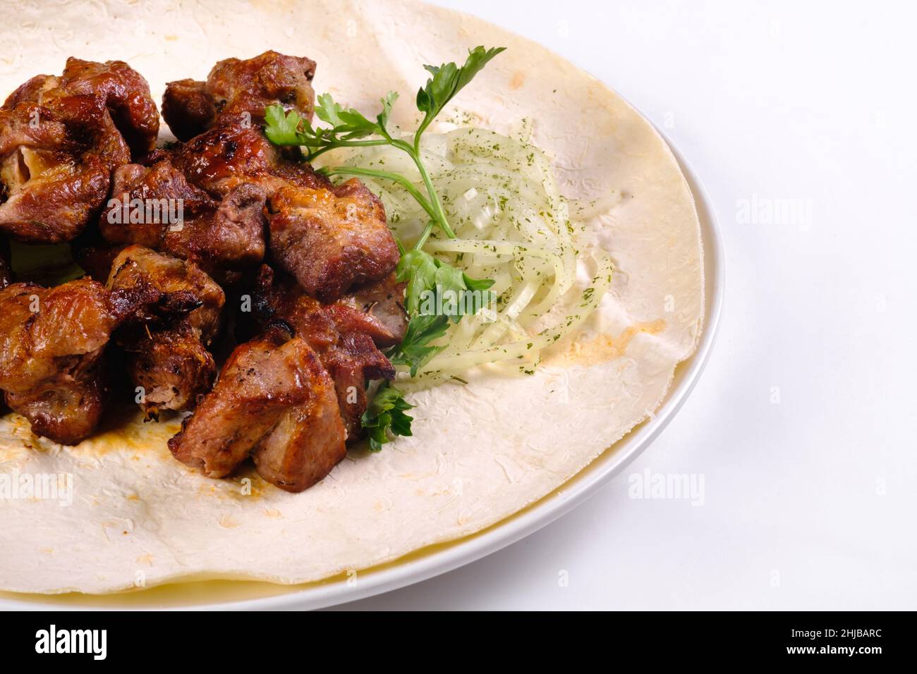 Le kebab de porc sur le lavash se trouve dans une assiette blanche sur un fond blanc isolé. Banque D'Images