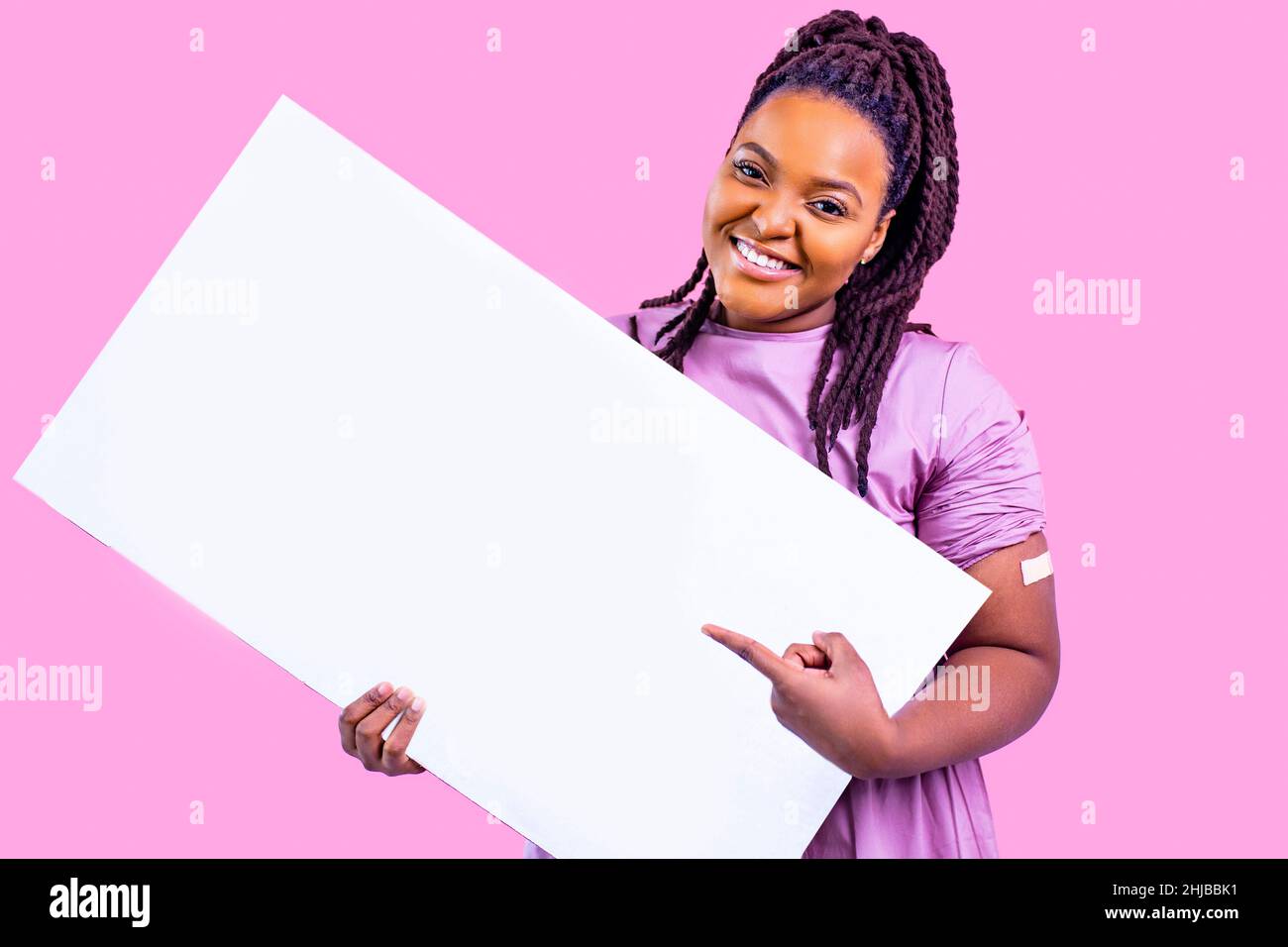 une femme positive se fait vacciner et tient une affiche blanche vide à la main avec du plâtre dans un espace de copie de studio rose Banque D'Images