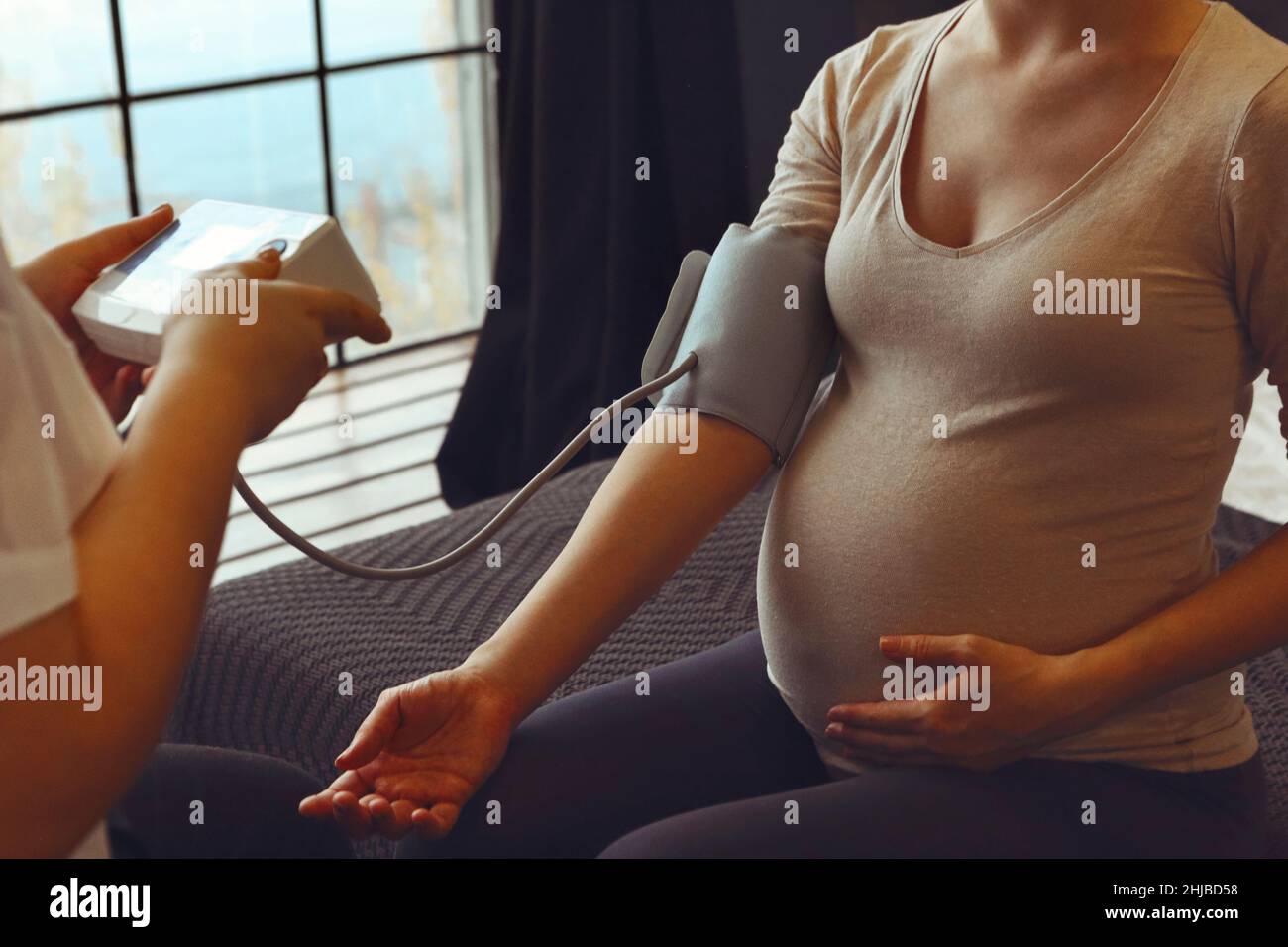 Médecin mesurant la pression artérielle de la femme enceinte lors de sa visite à la maison, thérapeute examinant la mère expectative pendant le rendez-vous de soins prénatals à Banque D'Images