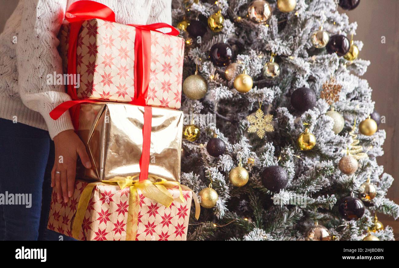 Coupe courte de femme tenant une pile de cadeaux de Noël ou du nouvel an pour les membres de la famille et les parents tout en se tenant près de firtree décoré, unreconnaisabl Banque D'Images