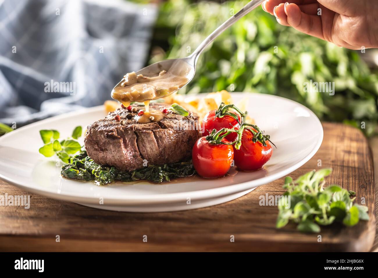 La sauce est versée sur un steak bien cuit servi sur un lit d'épinards avec des tomates cerises et des frites. Banque D'Images