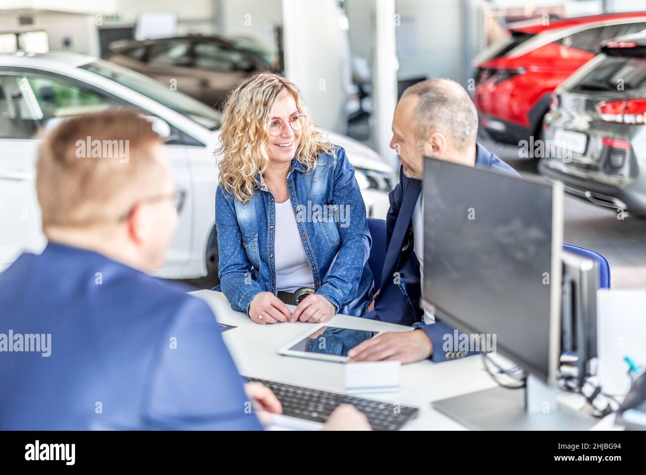 Mari et femme souriants se regardent les uns les autres et décident de la voiture qu'ils veulent s'asseoir à la table avec le directeur des ventes. Banque D'Images