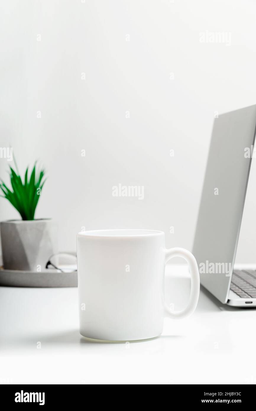 Une tasse blanche se fond dans un espace de travail moderne et élégant avec un ordinateur portable.Maquette de tasse. Banque D'Images