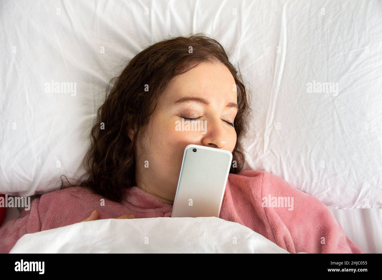 Photo en grand angle d'une jeune femme au lit avec le téléphone sur son visage Banque D'Images