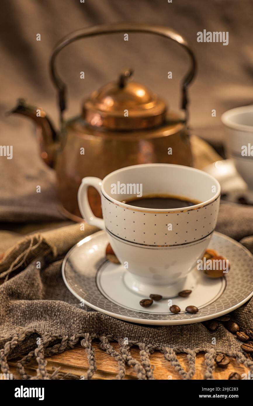 Deux tasses de café, théière en cuivre à l'arrière-plan, nuances de marron et de gris, tissu en nuances de gris Banque D'Images
