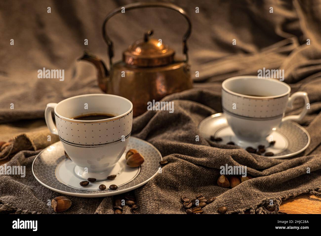 Deux tasses de café, théière en cuivre à l'arrière-plan, nuances de marron et de gris, tissu en nuances de gris Banque D'Images