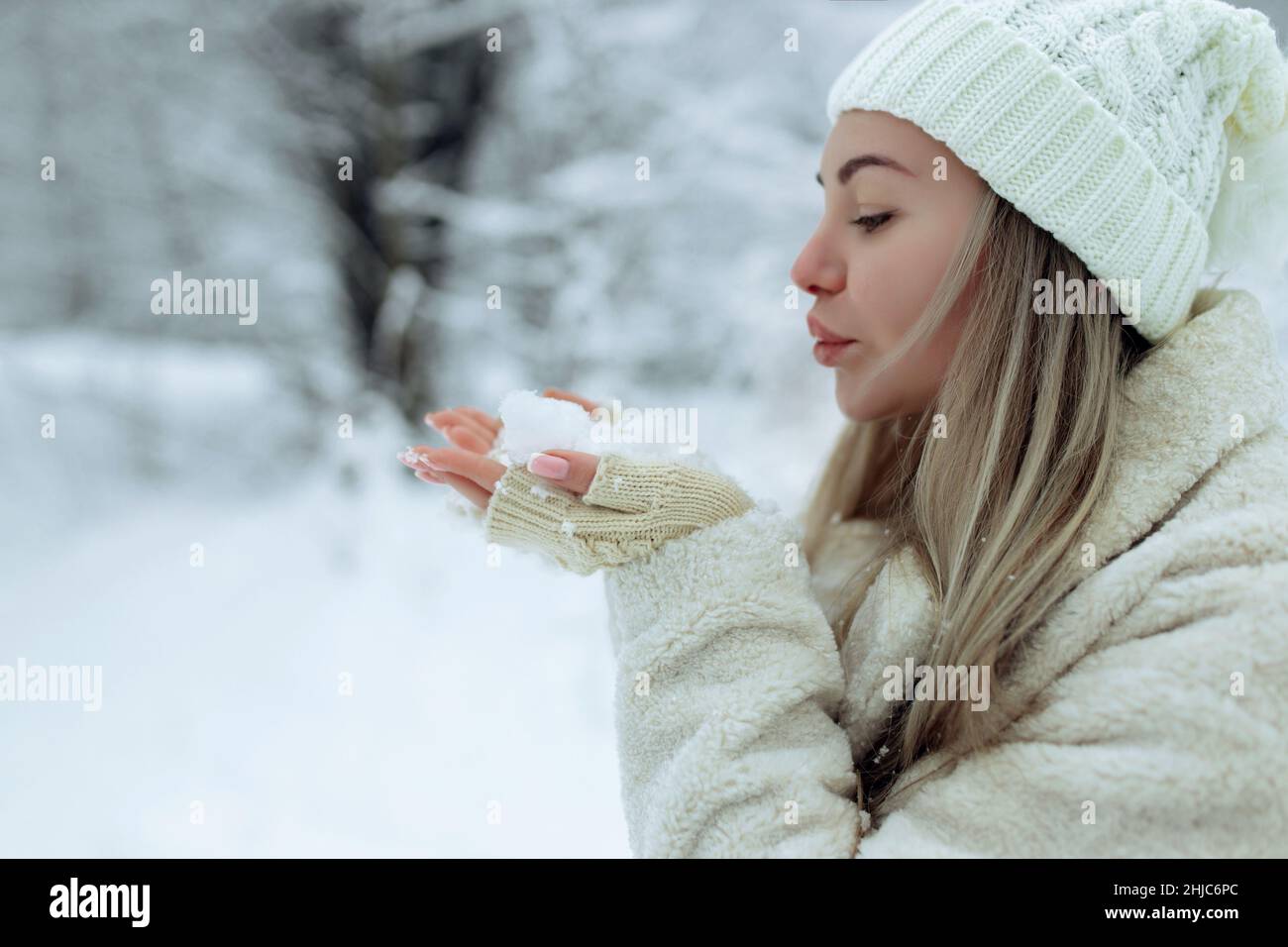 Belle fille en vêtements d'hiver tendance souffle la neige des paumes de ses mains.Joie à la première neige. Jeune blonde dans un chapeau blanc dans une neige Banque D'Images