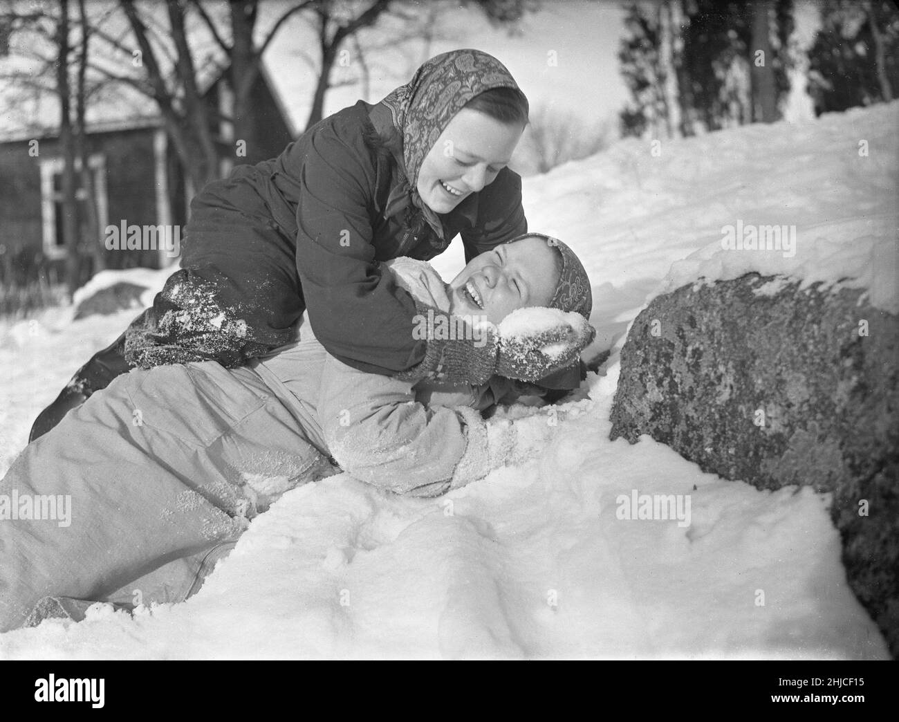 Hiver en 1940s.Les deux filles jouent dans la neige en riant.L'un au-dessus de l'autre mettant de la neige dans son visage.Ils travaillent dans une ferme en Suède pendant la Seconde Guerre mondiale et ont occupé le rôle de travailleurs masculins lorsqu'ils étaient dans l'armée suédoise et souvent placés à la frontière suédoise très loin.Rotebro Suède février 1940.Kristoffersson réf. 78-3 Banque D'Images