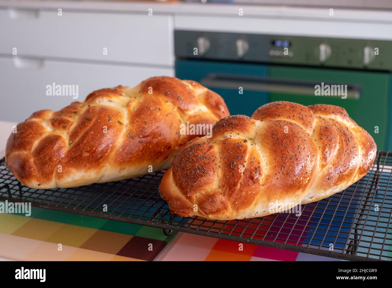 Deux pains de Challah traditionnels, cuits à la maison, rafraîchis sur un plateau en fil métallique. L'un est recouvert de graines de pavot et l'autre de romarin. Banque D'Images