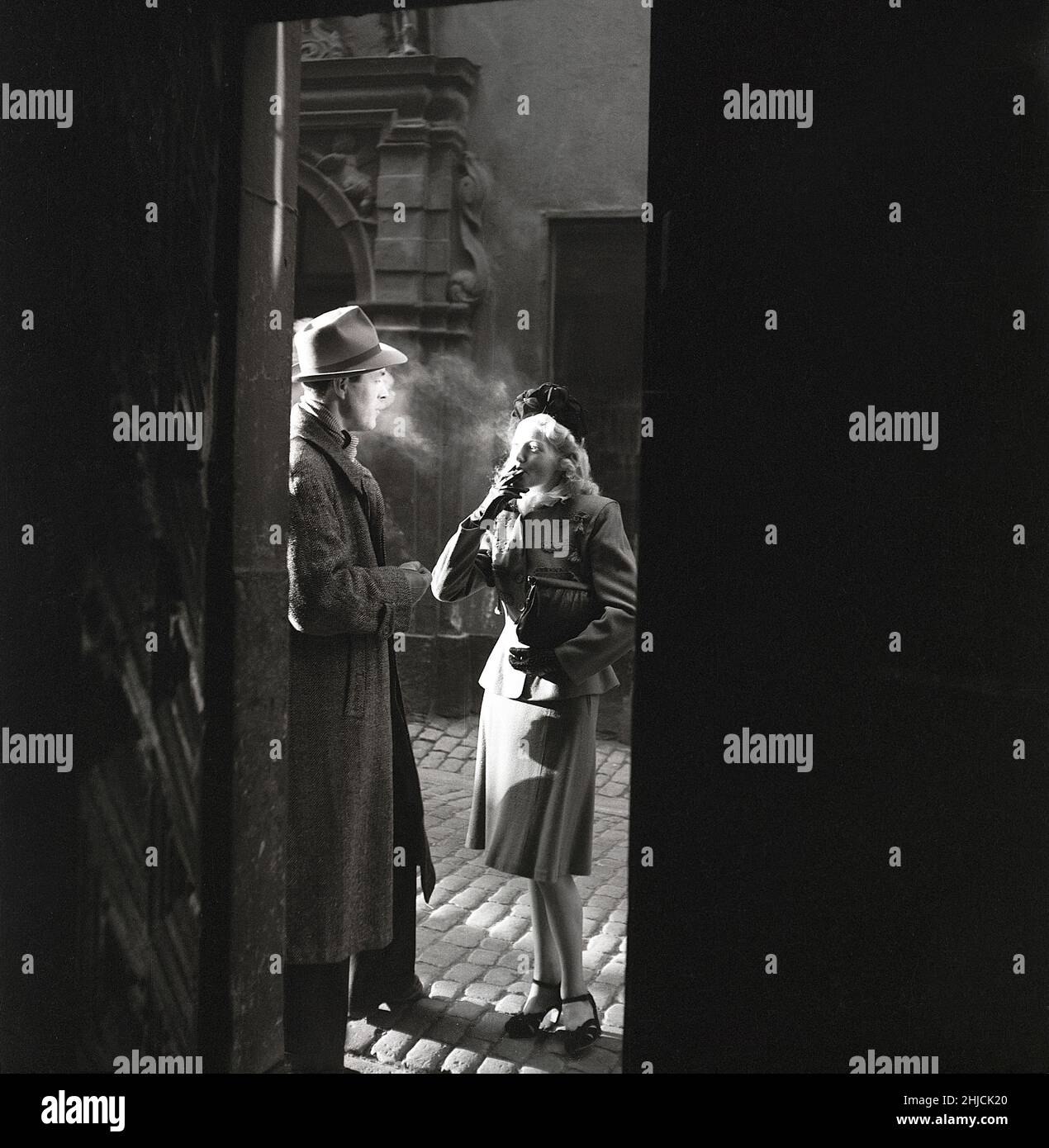 1940s couple.Un couple photographié le soir au soleil dans une vieille rue qui fume une cigarette.Ce sont les acteurs Karl-Arne Holmsten et Irene Söderblom qui prennent une pause dans le tournage du film Hotell Kåkbrinken.Suède 1946.Photo Kristoffersson Y6-5 Banque D'Images