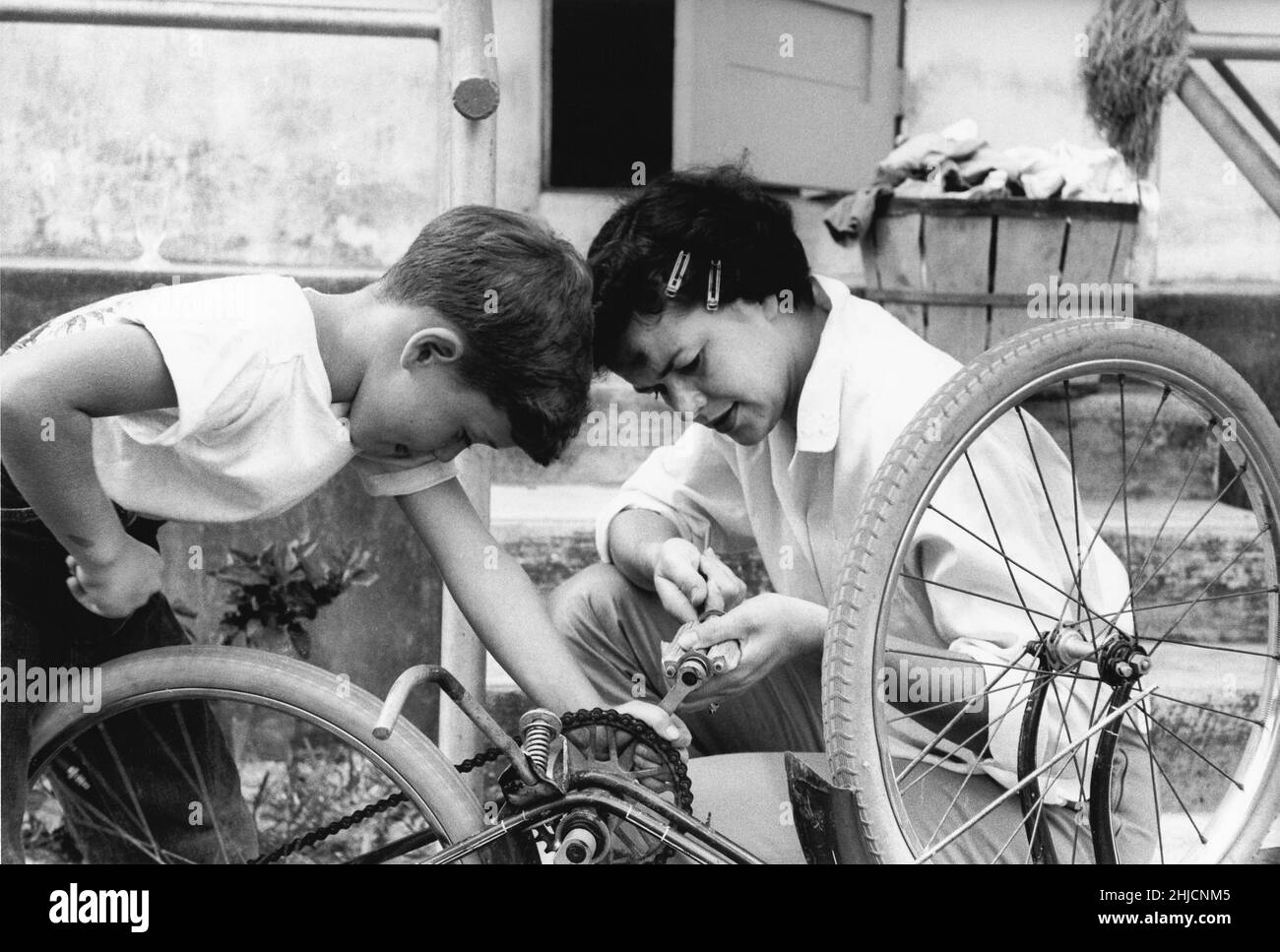 Photographie en noir et blanc d'une mère qui aide son fils à fixer sa bicyclette.Photographie tirée d'un magazine historique Cosmo.1960s. Banque D'Images