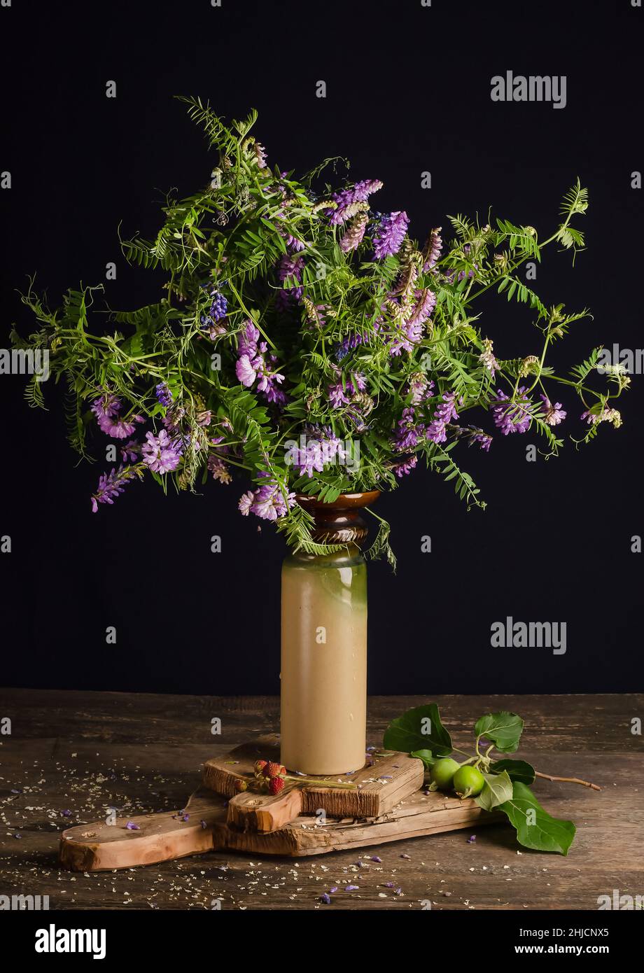 Encore la vie avec un bouquet de fleurs de champ d'été de pois de souris dans un vase sur un fond noir sur une ancienne table en bois vintage. Banque D'Images