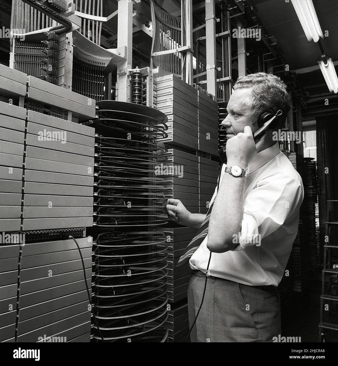 Téléphonie dans le 1970s.Homme dans une pièce avec un tableau de commutation automatique reliant les appels via un dispositif mécanique qui connecte les pièces d'appel et de réception.Le fabricant est LM Ericsson.Suède 1971 Kristoffersson ref. Ed Banque D'Images