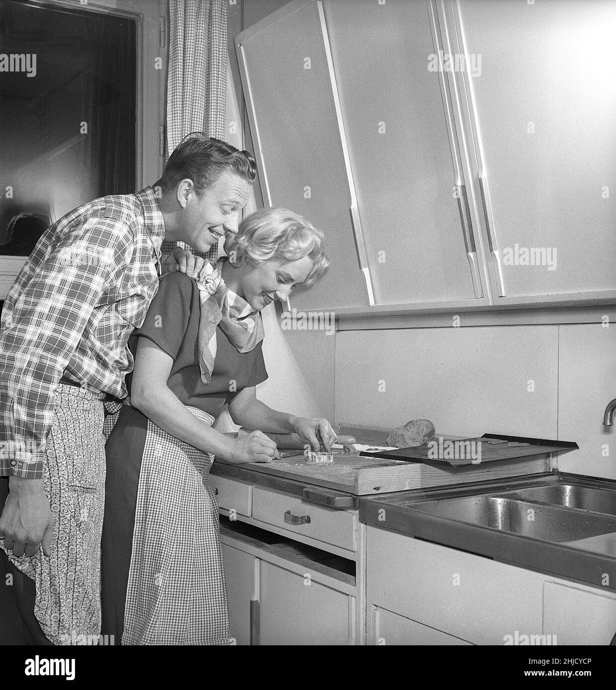 Dans la cuisine dans le 1950s.Ajeune couple qui fait cuire des biscuits de pain d'épice en forme de coeur pour noël.Elle met la forme de métal en forme de cœur sur la pâte pour faire la forme.Elle est actrice UllaCarin Rydén.Suède 1951. Réf. Kristoffersson BE65-9 Banque D'Images