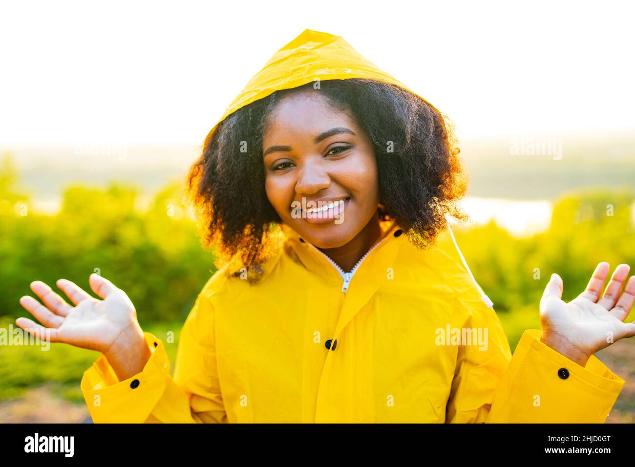 afro amrican femme curly cheveux porter un imperméable jaune et regarder la caméra lumière du coucher de soleil extérieur Banque D'Images