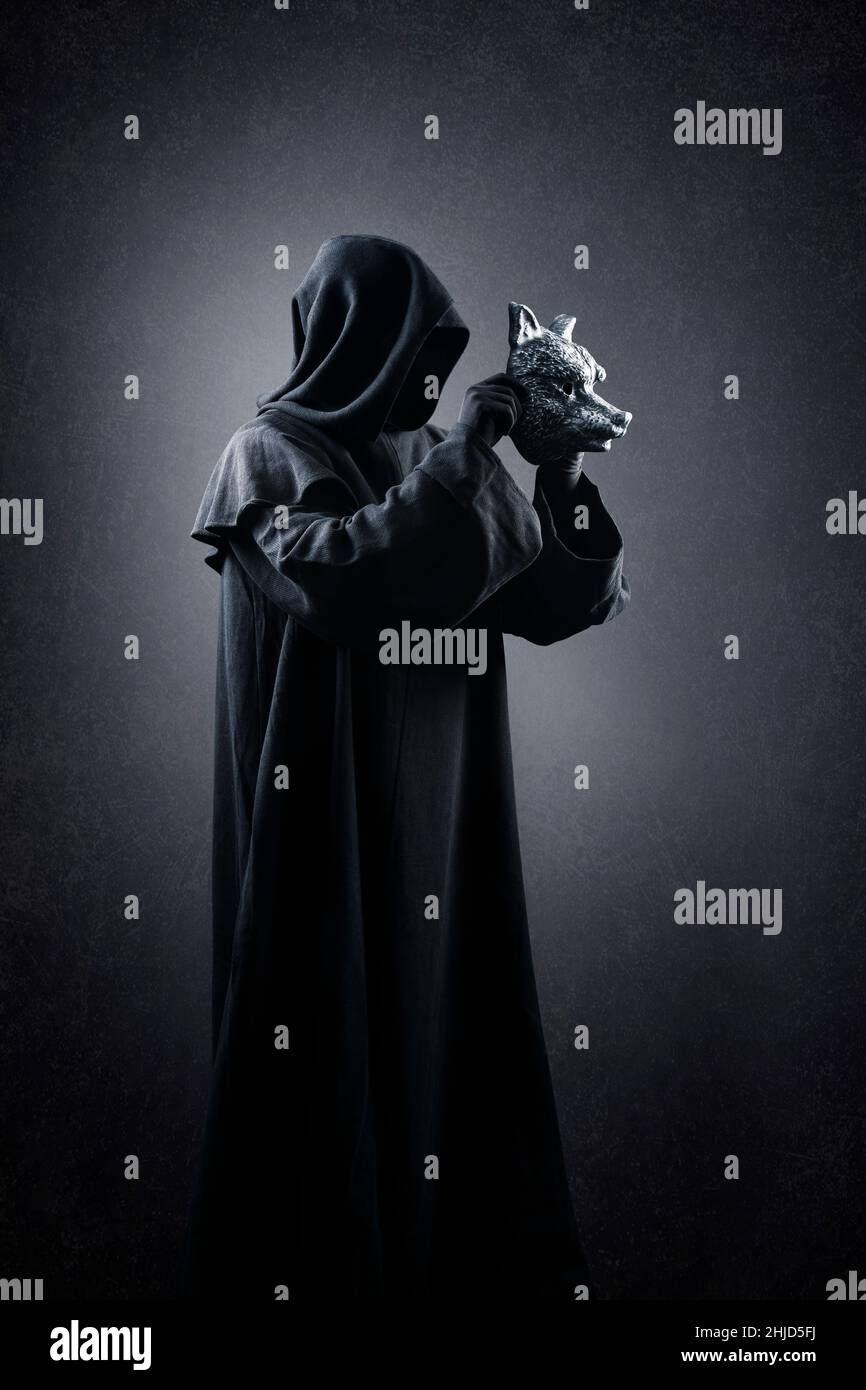 Personnage créepy en manteau à capuchon avec masque de loup dans les mains sur fond sombre et brumeux Banque D'Images