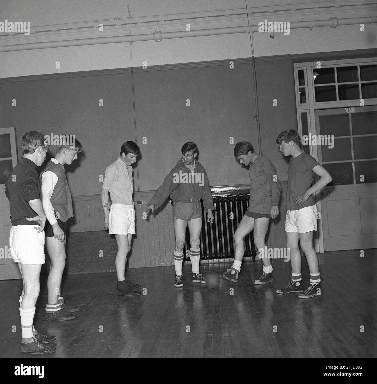 1960s, historique, club de jeunes, adolescents en kit de gym et pompes, avec un petit ballon, dans une salle de sport avec un entraîneur masculin, Écosse, Royaume-Uni. Banque D'Images