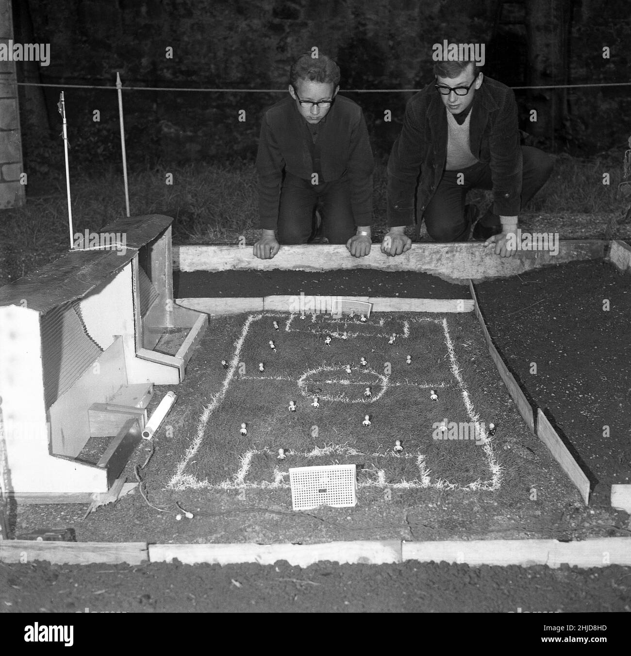 1960s, historique, deux adolescents s'agenouillent à côté d'un terrain de football miniature et d'une tribune dans un village modèle, un projet scolaire. Banque D'Images