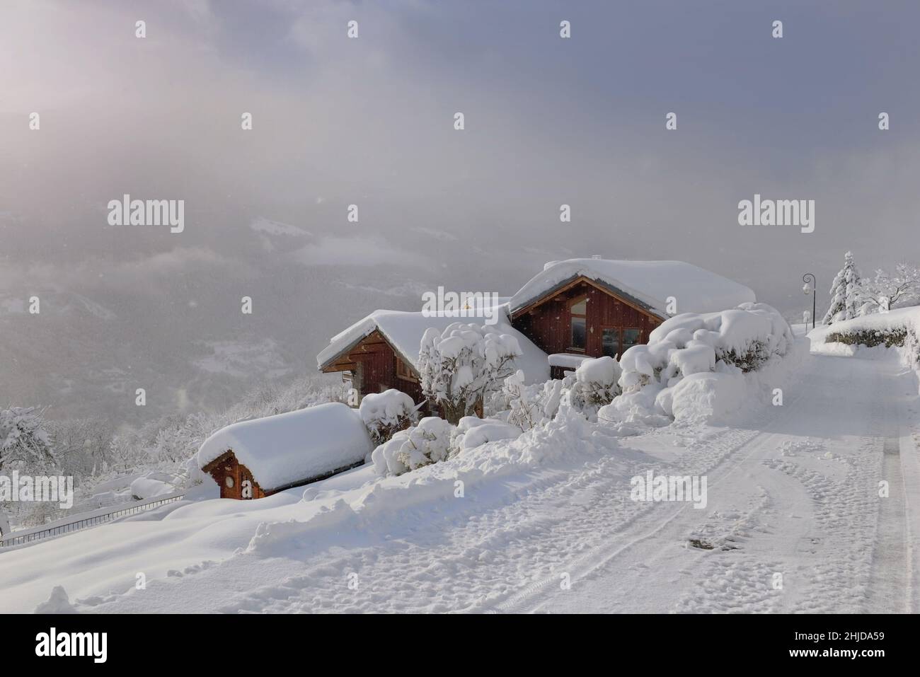 les chalets en bois dans le village alpin couvraient le bord d'une route rurale blanche Banque D'Images