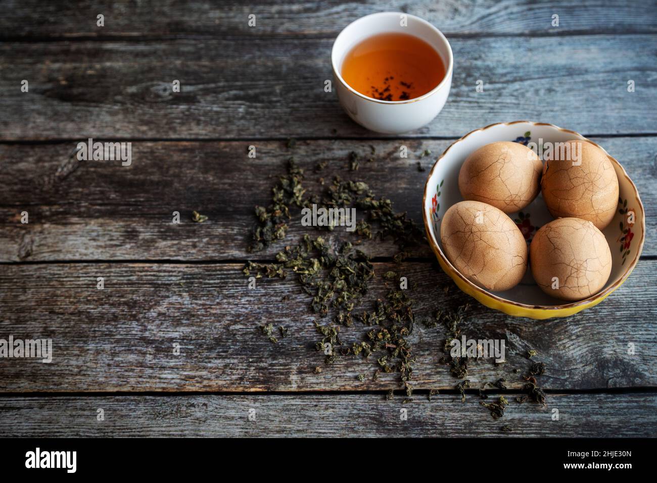 Des œufs de thé épicés en marbre chinois dur sur une table rustique en bois avec des feuilles de thé et une tasse de thé chinois en arrière-plan. Banque D'Images