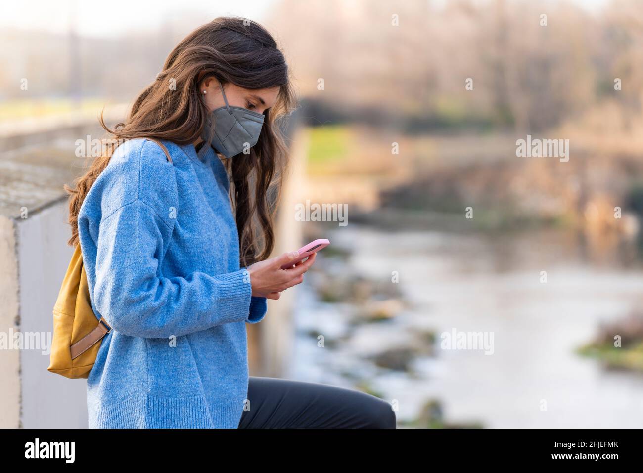 Jeune fille avec masque gris regardant le téléphone en marchant dans le parc Banque D'Images