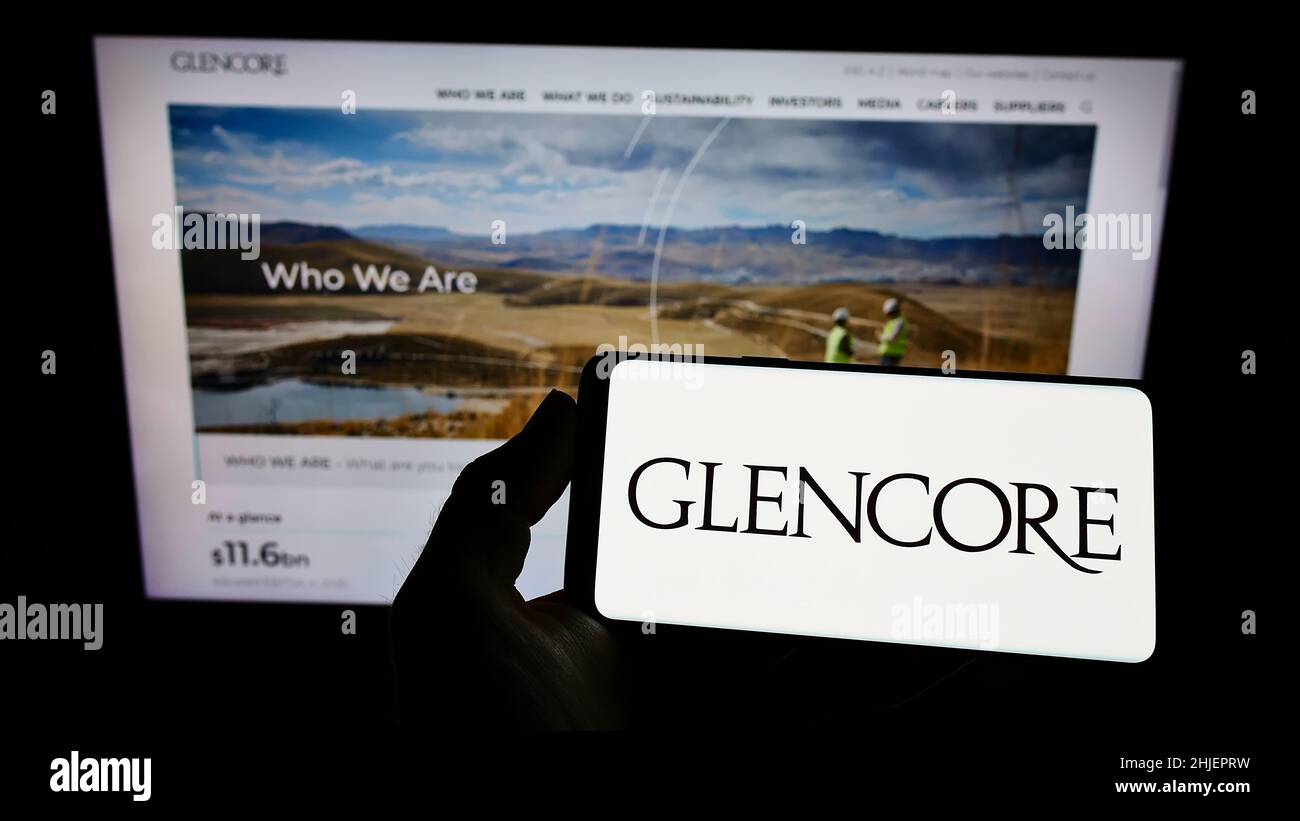 Personne détenant un smartphone avec le logo de la société de commerce de marchandises Glencore plc à l'écran devant le site Web.Mise au point sur l'affichage du téléphone. Banque D'Images