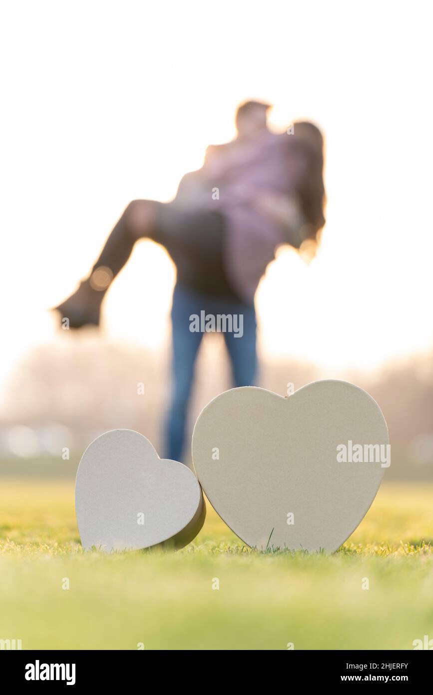 Un jeune couple enserre derrière deux formes de coeur dans un parc le jour de la Saint-Valentin Banque D'Images