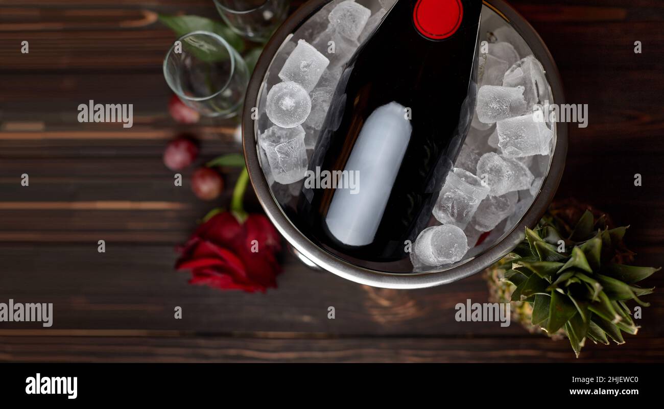 Bouteille de champagne dans un seau avec glace, rose, ananas et verres, sur fond de bois avec espace pour le texte Banque D'Images