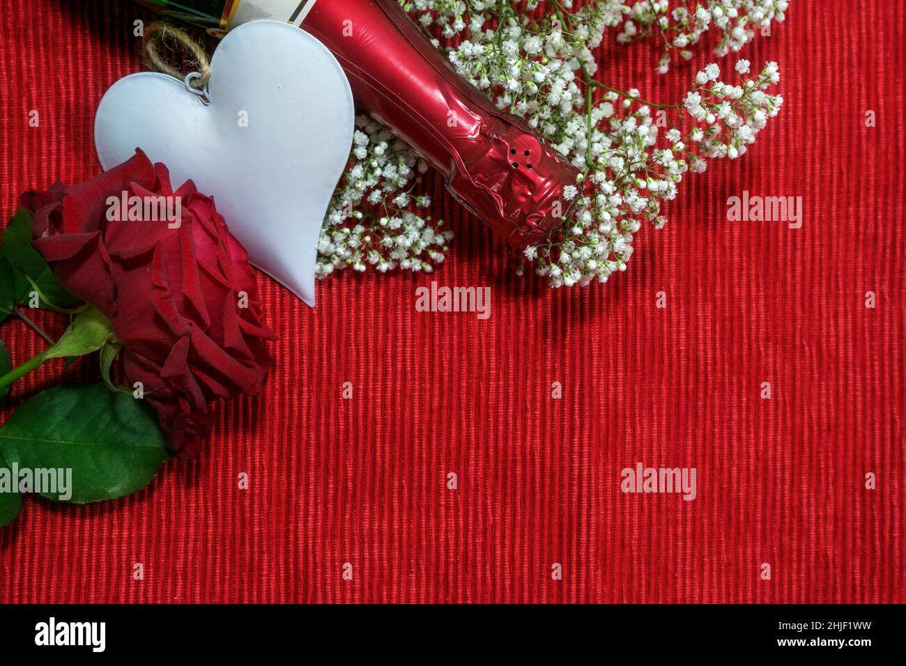 Bouteille de champagne, rose, forme de coeur et fleurs sur fond de tissu rouge, concept d'amour pour la Saint Valentin, espace de copie, vue d'en haut Banque D'Images