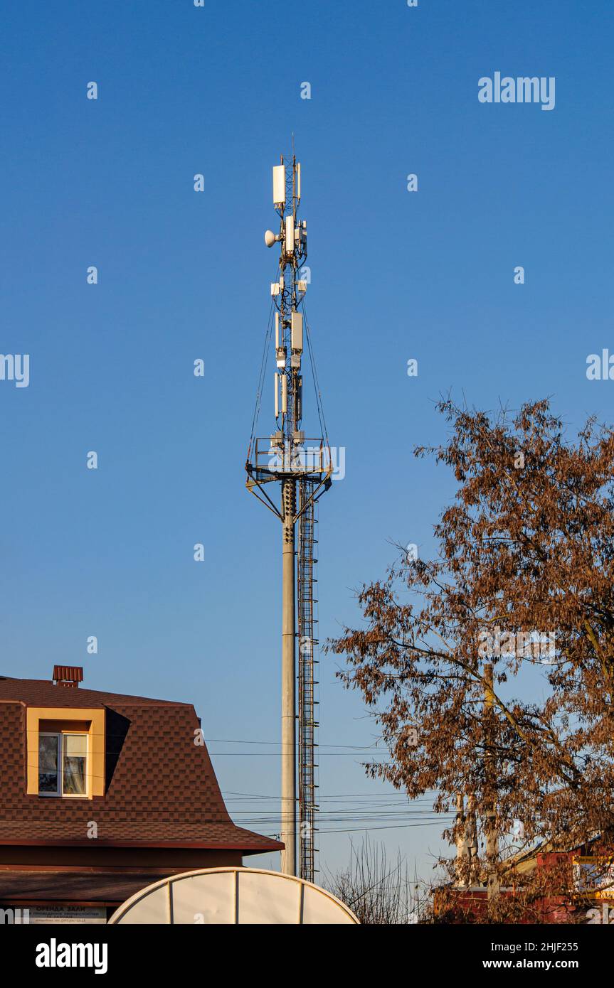 Une tour à cellules hautes avec des antennes sur le dessus, dans une ville près de bâtiments résidentiels, contre un ciel clair. Banque D'Images