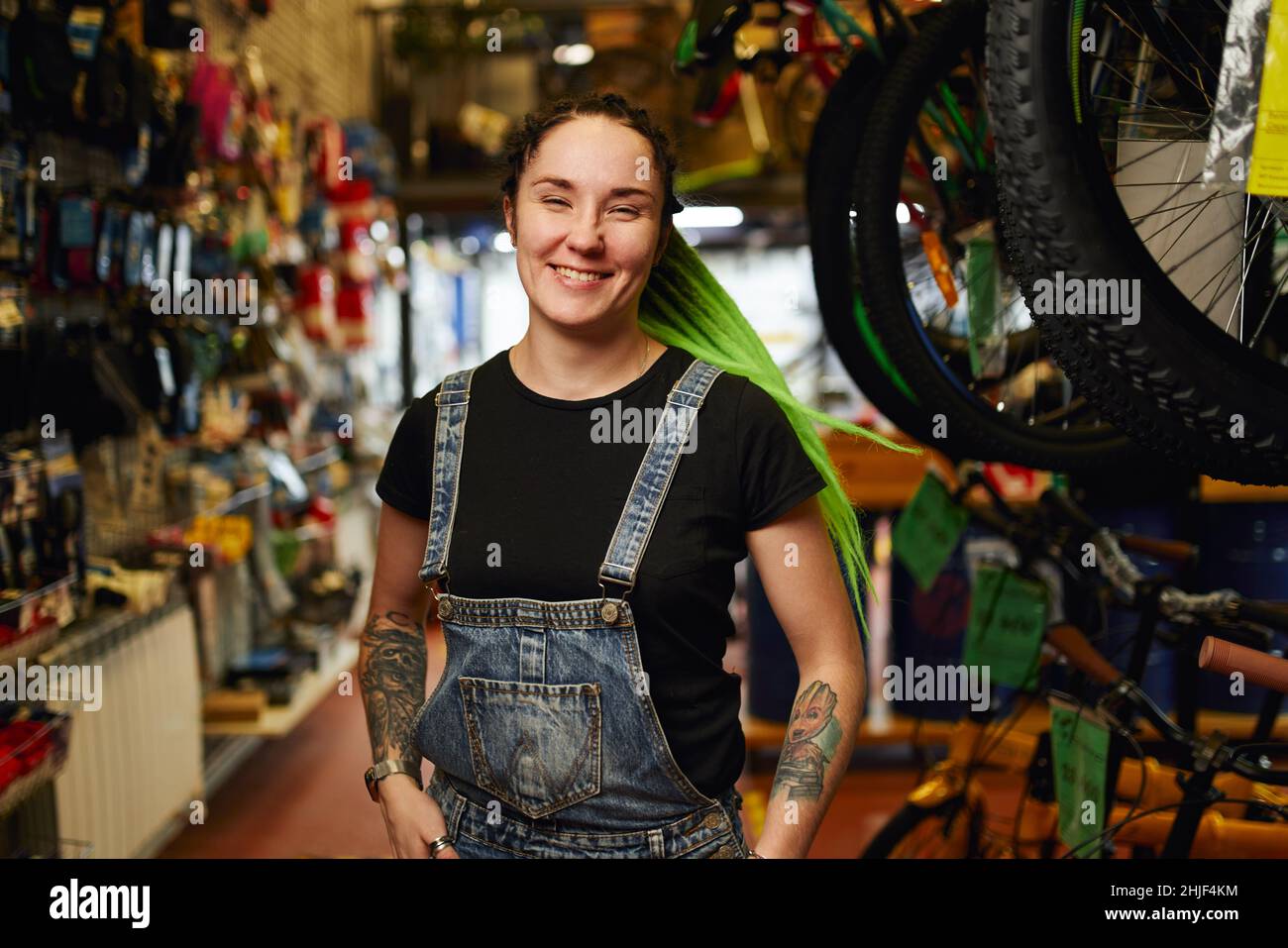 Femme joyeuse vendeur en denim général avec tatouages sur des dreadlocks lumineux debout sur le marché vendant des biens d'accueil Banque D'Images