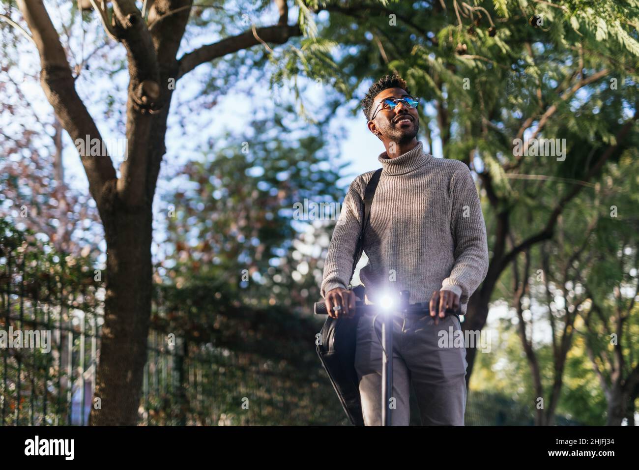 Homme afro-américain avec un gilet à col roulé en train de faire une promenade avec son scooter électrique dans un parc Banque D'Images