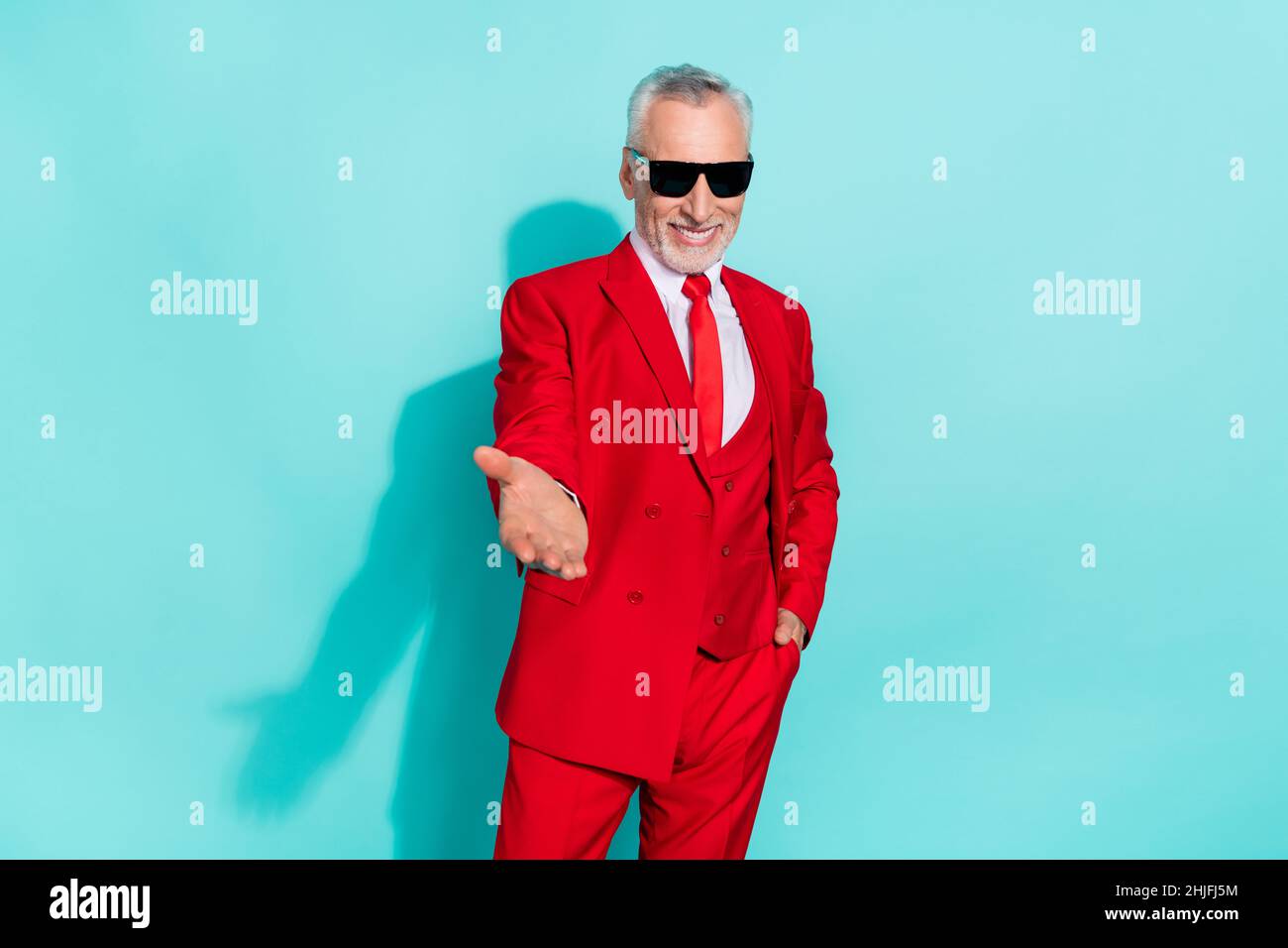 Photo de sympathique retraité homme porter un costume rouge trois pièces lunettes sombres vous donnant bras isolé couleur turquoise arrière-plan Banque D'Images