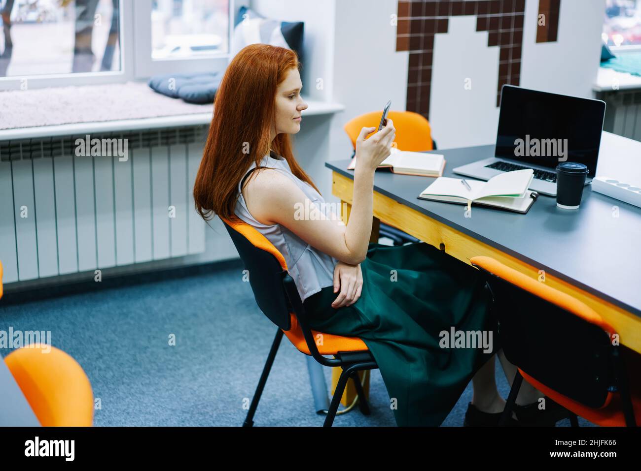 Femme vérifiant un smartphone lors de l'utilisation d'un ordinateur et d'un ordinateur portable Banque D'Images